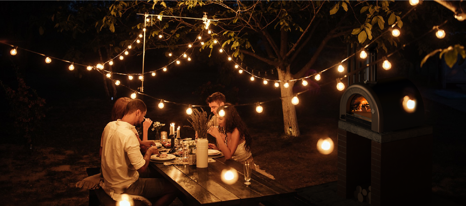 table of people sharing a meal cooked with Forno Venetzia's oven in the evening under small lights that warm the atmosphere